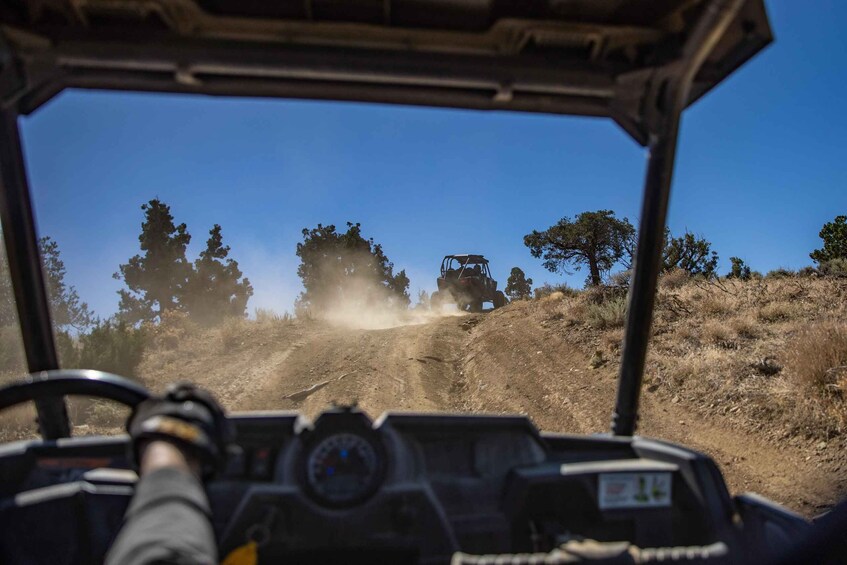 A vehicle driving on a dirt road with trees and hills in the background. 3