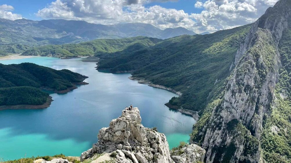 A mountainous landscape with a turquoise lake surrounded by lush greenery and rocky cliffs. 1