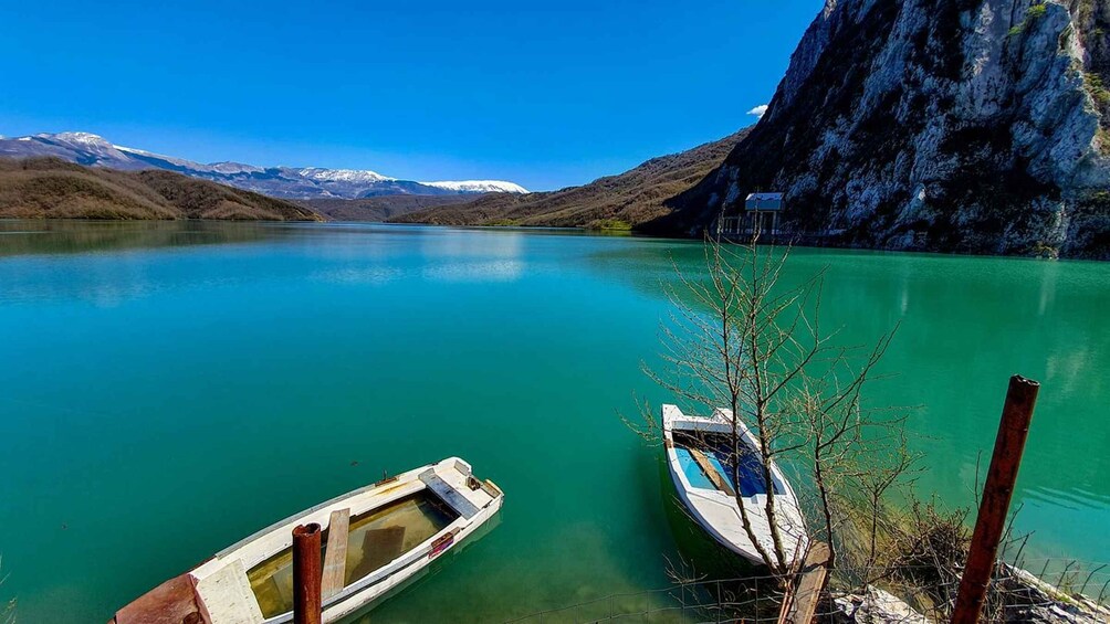 A calm lake with boats docked, surrounded by mountains and clear skies. 2