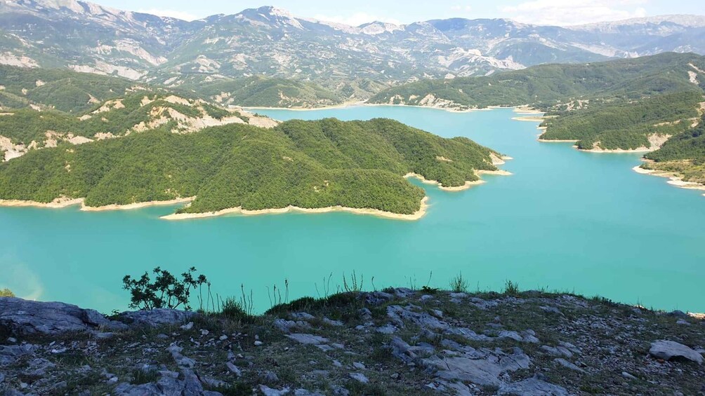 A mountainous landscape with a turquoise lake surrounded by forested hills. 3