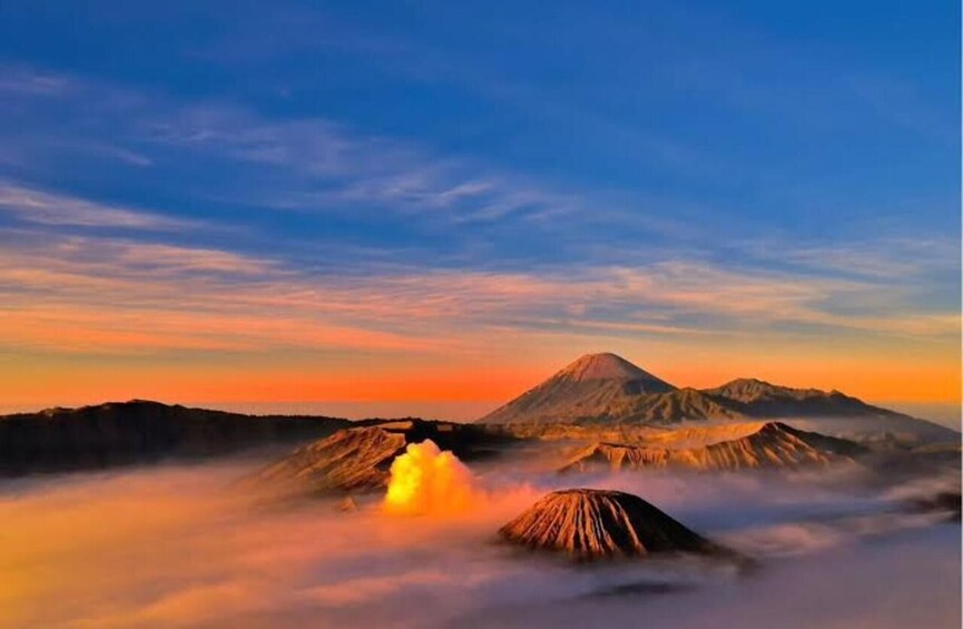 A volcano with an active eruption, surrounded by clouds and a sunset sky. 3