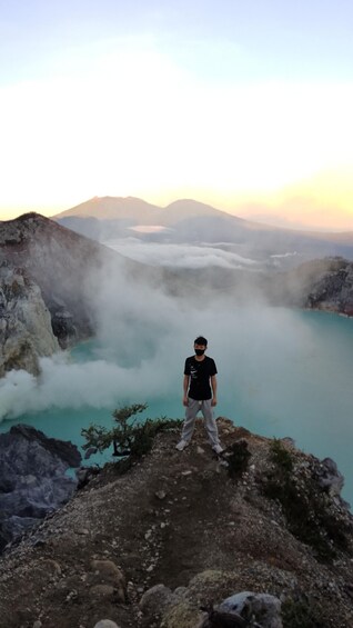 A person standing on a rocky outcrop overlooking a turquoise lake with mist and mountains in the background. 5