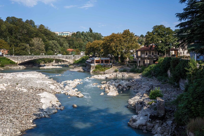 A river with a stone bridge, buildings, and a hillside. 3
