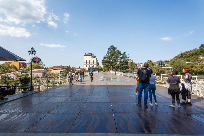 A pedestrian bridge with people walking, a lamppost, and buildings in the background. 4