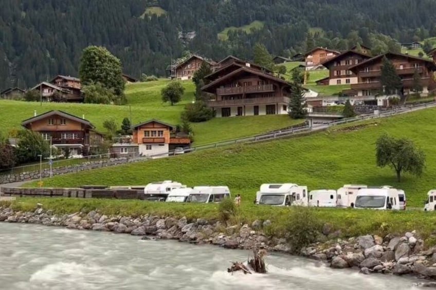 A river with white water rapids, surrounded by green hills and wooden chalets. 3