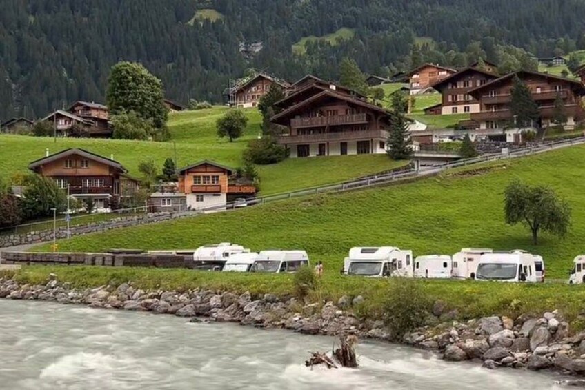 A river with white water rapids, surrounded by green hills and wooden chalets. 3