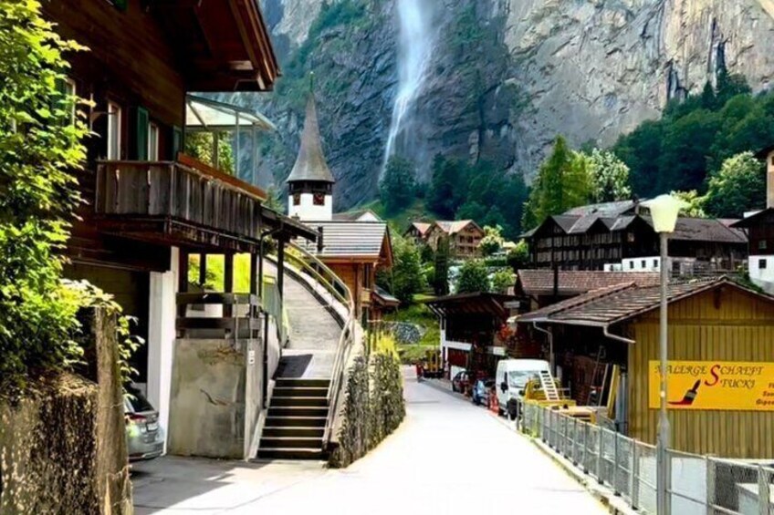A mountain village with wooden buildings, a church, and a waterfall. 1