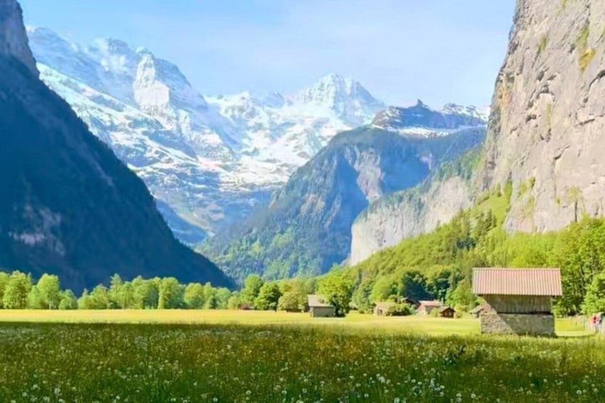 A valley with a small house, lush greenery, and snow-capped mountains. 4