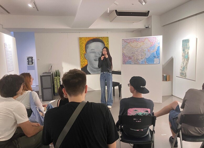 A group of people in a modern art gallery with a large portrait and a map on the walls. 3