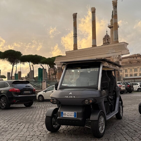 A black ALBA electric vehicle parked on cobblestone with a cityscape and historical architecture in the background. 2