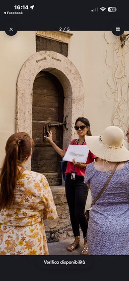 A person standing in front of an old wooden door with a sign above it, holding a white folder. 5