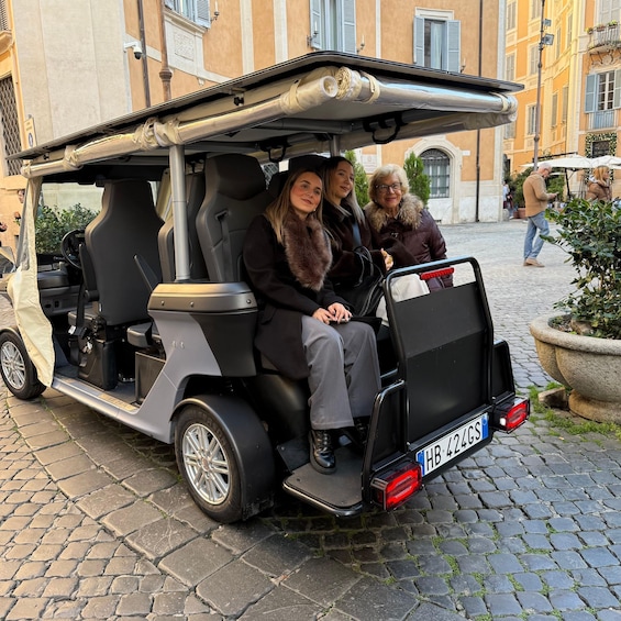 A vintage golf cart with two passengers, parked on cobblestone street. 5
