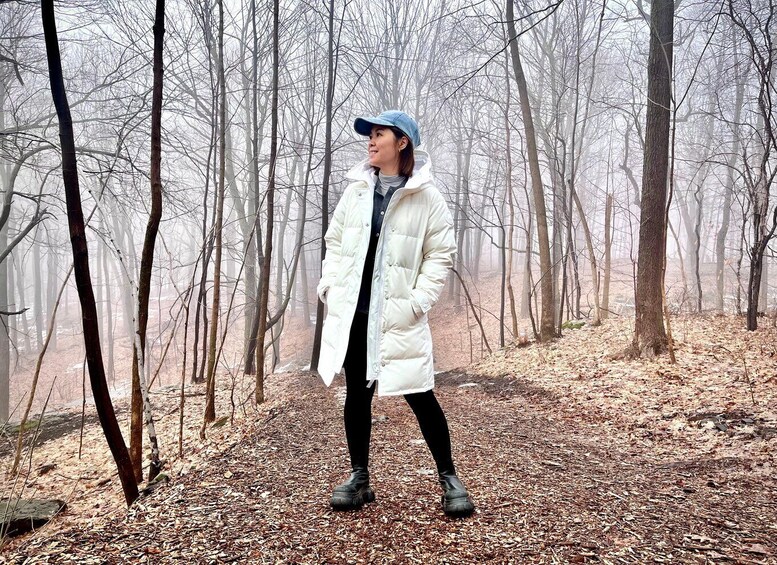 A person standing in a forest with leaf-covered ground and bare trees. 4