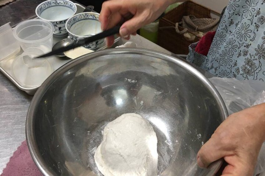 A person mixing dough in a metal bowl with a spoon. 3