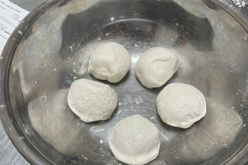 A stainless steel bowl with five white dough balls. 2