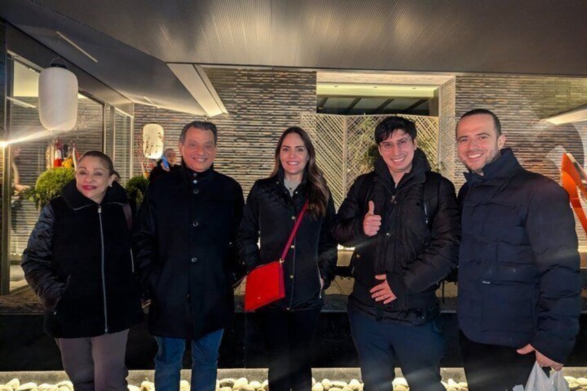 A group of people standing indoors with a modern interior design, including a patterned wall and a glass barrier. 2