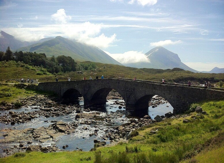 A stone bridge over a rocky stream with mountains in the background. 5