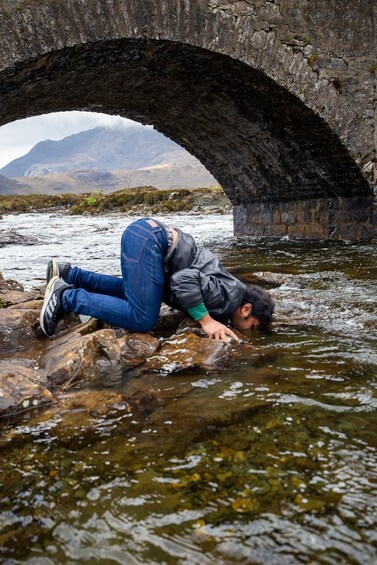 A person resting under a stone bridge over a river. 2