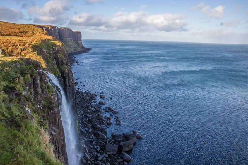 A coastal landscape with a waterfall, rocky shore, and cliffs. 3