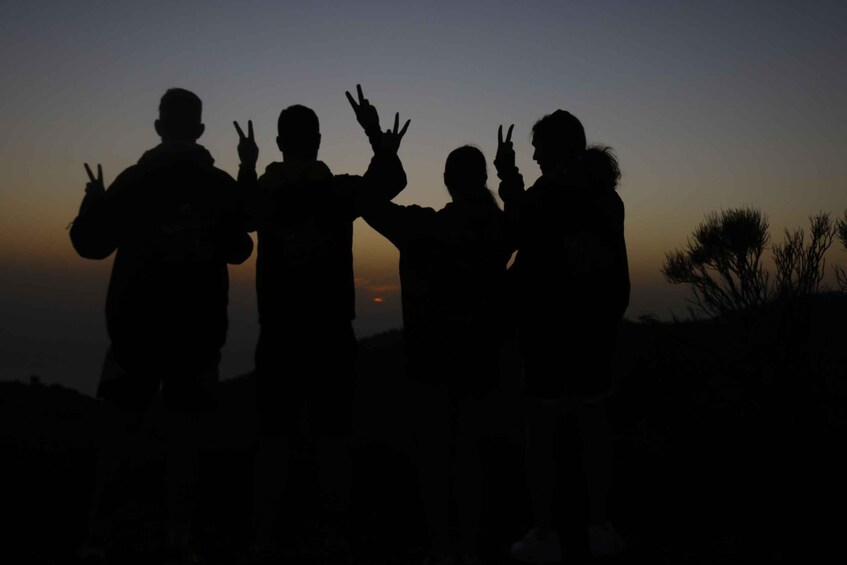 Silhouettes of people making peace signs against a sunset. 2