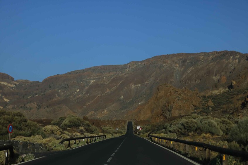 A road leading through a mountainous landscape with guardrails and a clear blue sky. 3
