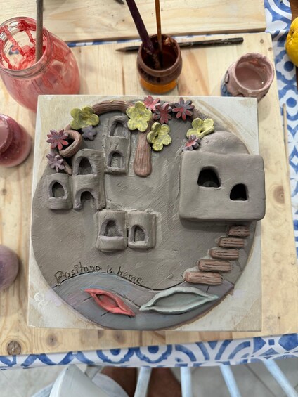 A ceramic artwork with a house, trees, and a path. 4