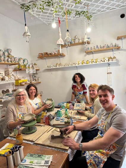 A pottery workshop with shelves of ceramic items and people working on pottery. 5