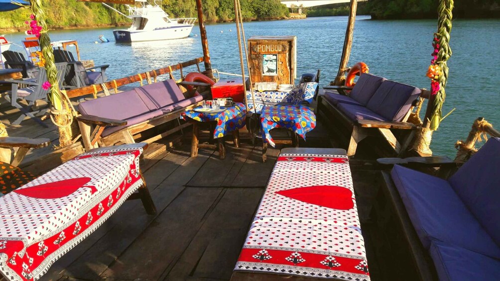 A wooden deck with lounge chairs and tables, a boat docked in the background, and a sign reading 'POMBOO.' 1
