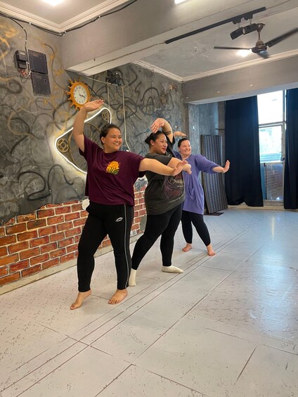 Three people performing a synchronized exercise routine in a room with a graffiti wall and a large clock. 5