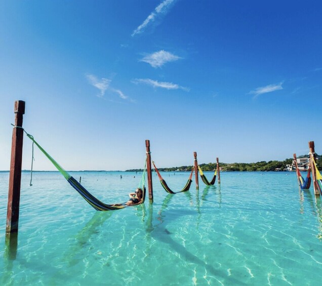 A hammock tied between wooden posts in clear turquoise water, with a person relaxing in it. 1