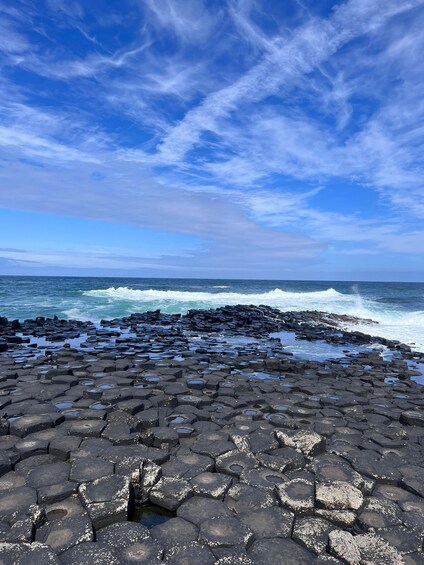 A rocky coastline with hexagonal basalt formations and waves crashing against the rocks. 3