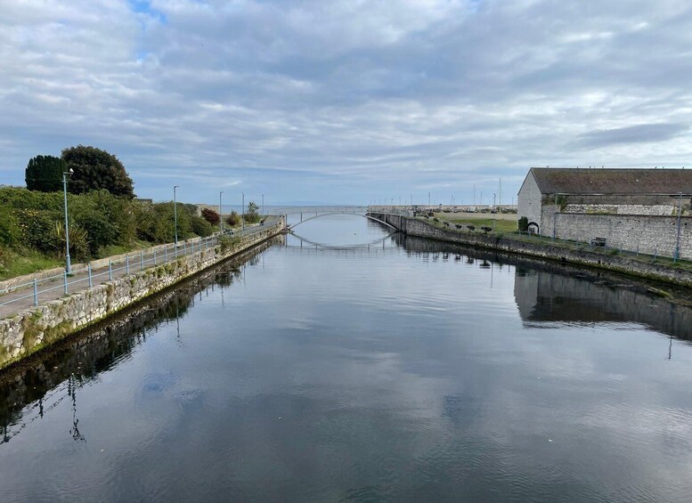 A calm canal with a stone wall on one side and a bridge in the distance. 4