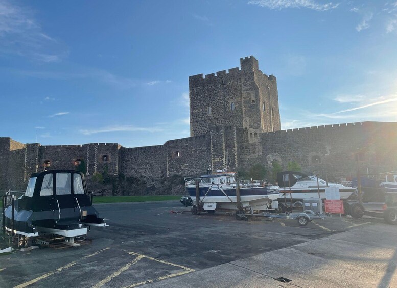 A historic stone castle with a tower, a parking lot with boats, and a black vehicle. 5