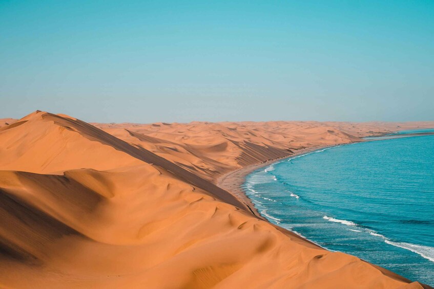 A desert landscape with sand dunes and a turquoise sea. 1