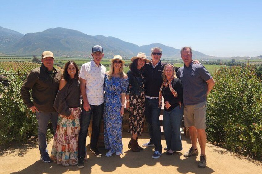 A group of people standing in a vineyard with mountains in the background. 2