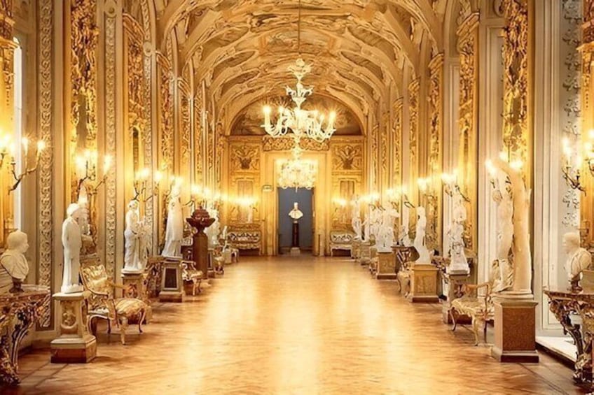 An opulent hallway with ornate gold detailing, statues, and a grand chandelier. 1