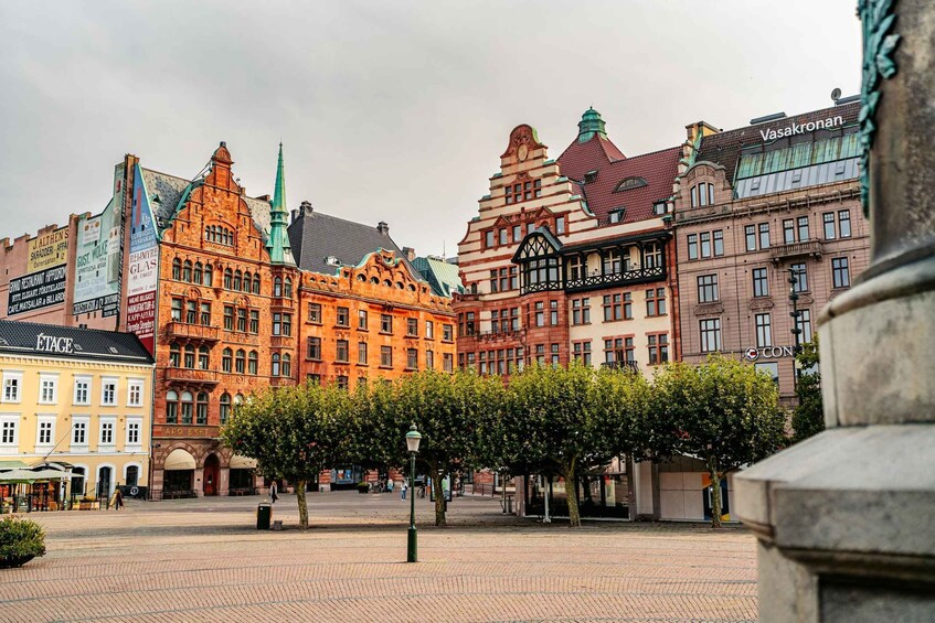 A historic European city square with ornate buildings and a central tree-lined area. 5