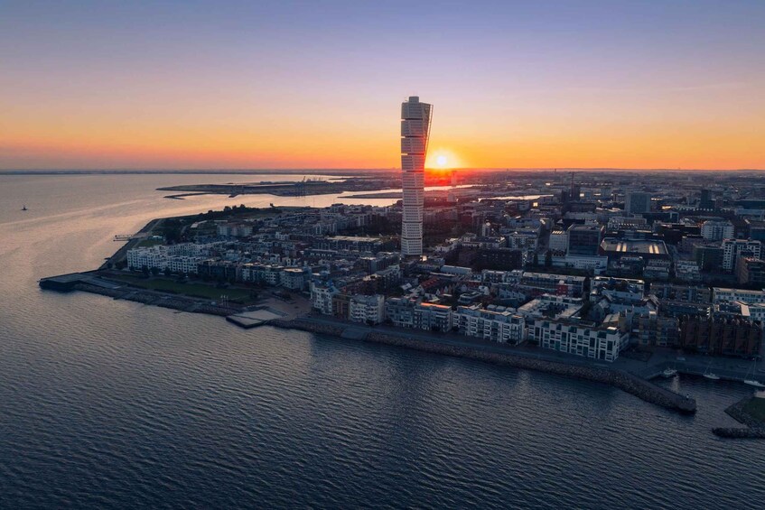A coastal cityscape with a prominent tower and a sunset over the water. 3