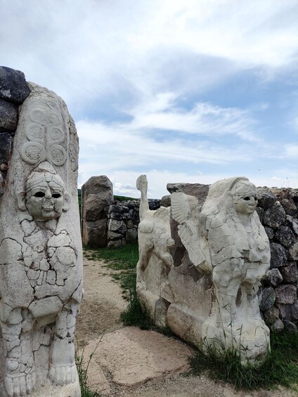 Ancient stone carvings of human figures and animals, set against a backdrop of stone walls and a clear sky. 4