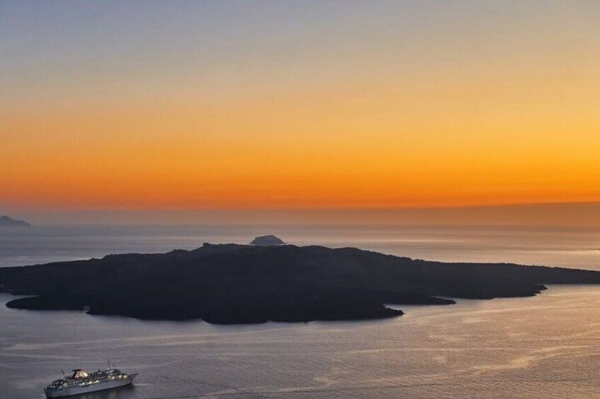 A sunset over a calm sea with a ship and an island silhouette. 3