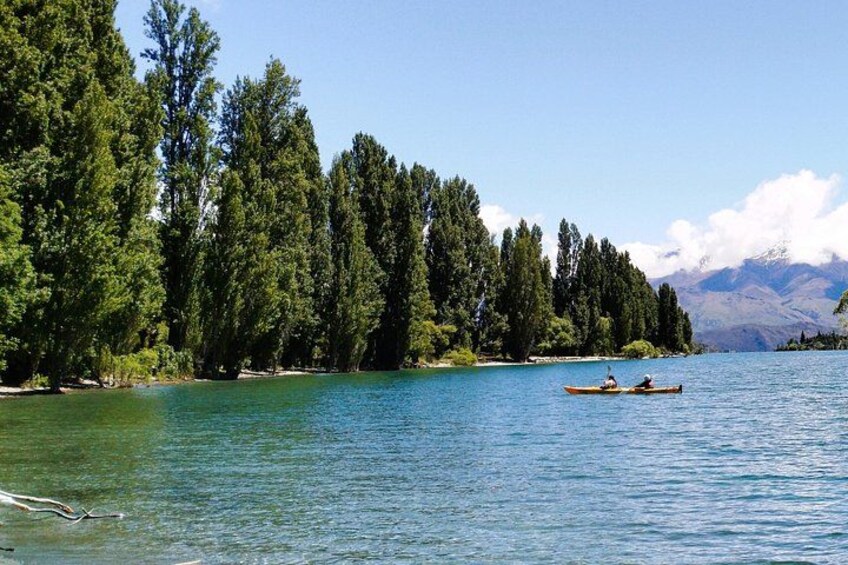 A calm lake surrounded by dense green trees, with two people kayaking in the distance. 2