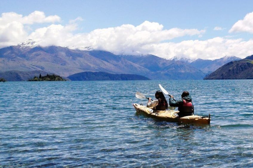 Two people kayaking on a calm lake with mountains in the background. 2