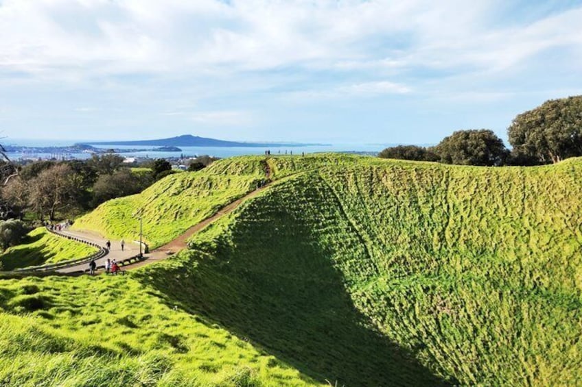 A green hill with a pathway and a distant view of the ocean. 1