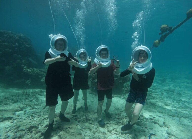 Four people underwater wearing diving helmets, surrounded by bubbles and a sandy seabed. 3