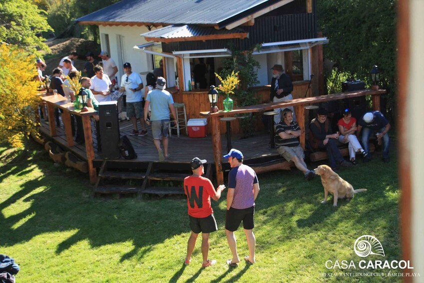 A wooden deck with people socializing, a dog, and a building with a sign reading 'CASA CARACOL.' 1
