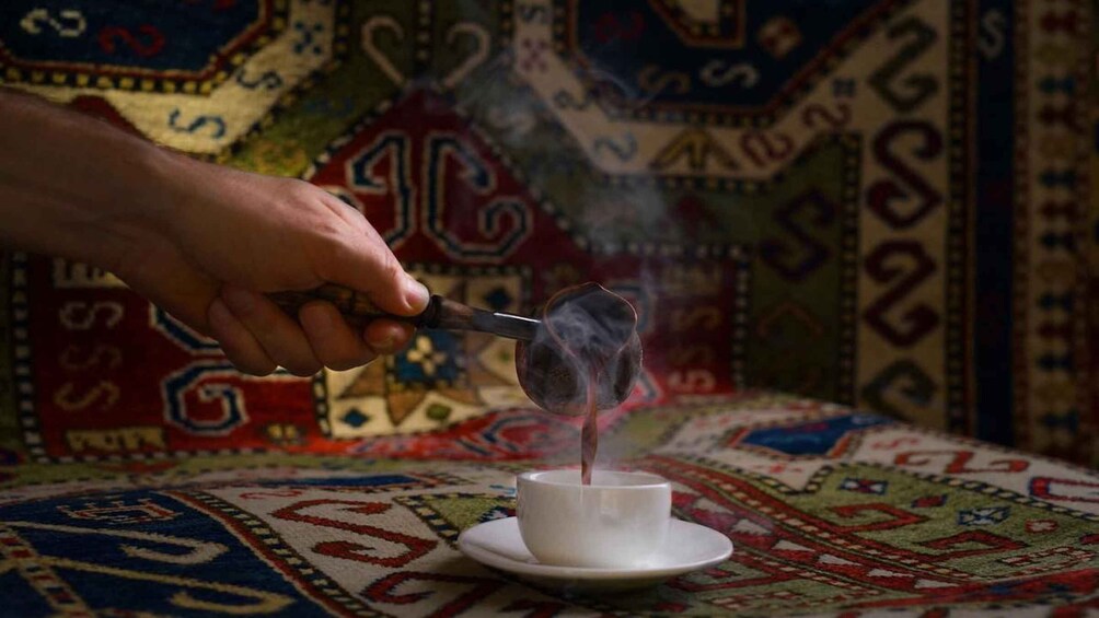 A hand holding a smoking device over a cup on a patterned tablecloth. 1