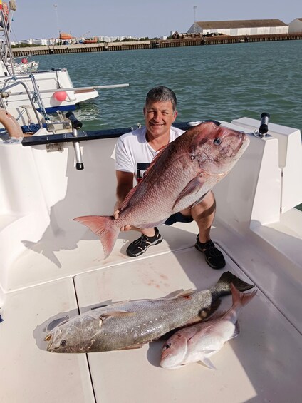 A man holding a large fish on a boat with two smaller fish on the deck. 4