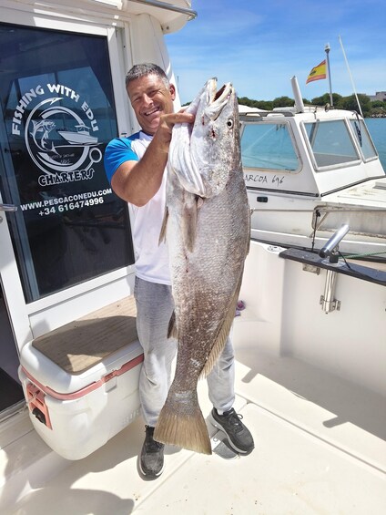 A person holding a large fish on a boat with a logo reading 'Fishing with Ed' and contact information. 5