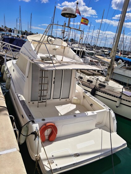 A white boat docked at a marina with other boats, a lifebuoy, and a flag. 2