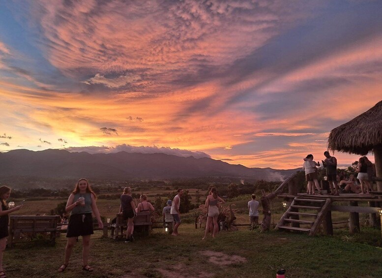A sunset over mountains with people gathered around a wooden structure. 4